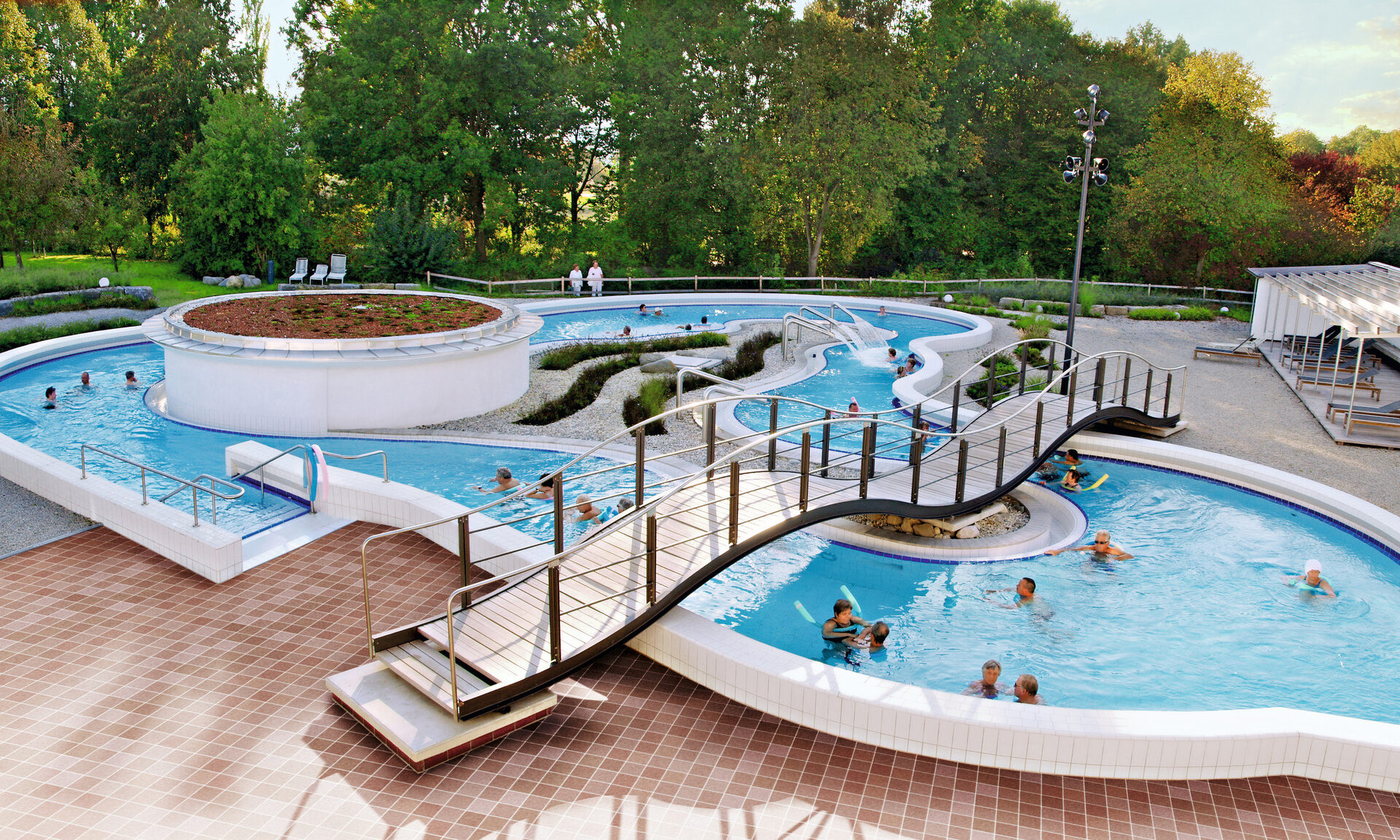 Blick auf das Schwimmbecken im Freien der Rottal Terme, mit vielen glücklichen Gästen die Badespass geniessen.