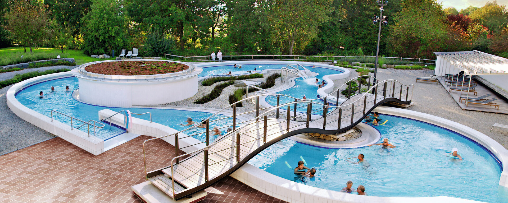 Blick auf das Schwimmbecken im Freien der Rottal Terme, mit vielen glücklichen Gästen die Badespass geniessen.
