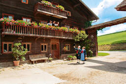 Zwei Besucher im Hofe vor einem alten Holzhaus in Bad Birnbach.