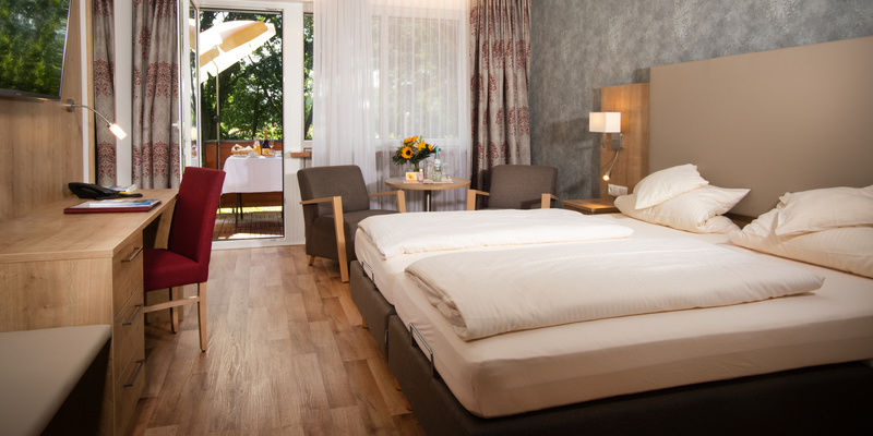 Der Schlafensbereich im komfortablen Doppelzimmer in Südlage des Hotel Quellenhof mit bequemen Doppelbett, Sitzecke und einem Schreibtisch.
