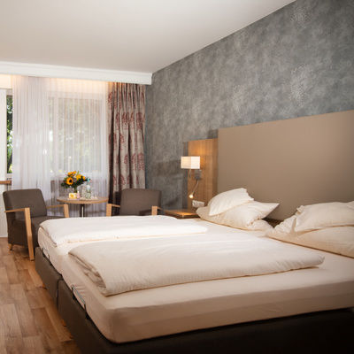 Der Schlafensbereich im komfortablen Doppelzimmer in Südlage des Hotel Quellenhof mit bequemen Doppelbett, Sitzecke und einem Schreibtisch.
