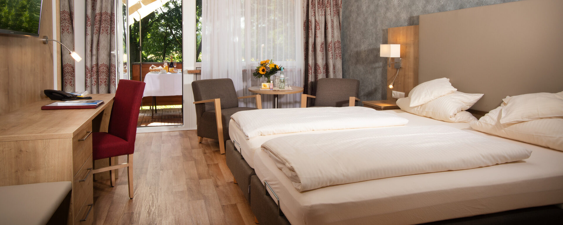 Der Schlafensbereich im komfortablen Doppelzimmer in Südlage des Hotel Quellenhof mit bequemen Doppelbett, Sitzecke und einem Schreibtisch.