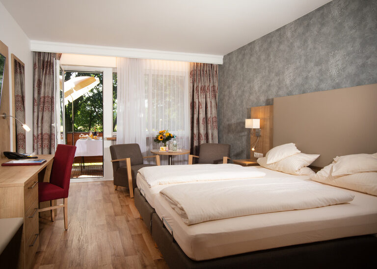 Der Schlafensbereich im komfortablen Doppelzimmer in Südlage des Hotel Quellenhof mit bequemen Doppelbett, Sitzecke und einem Schreibtisch.
