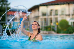 Eine lachende Frau spritz mit Wasser um sich in einem Becken in der Rottal Terme