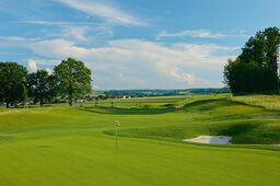 Eine sehr gut gepflegte Golffläche des Bella Vista Golfpark in Bad Birnbach an einem schönen Sommertag mit Bäumen und blauem Himmel.