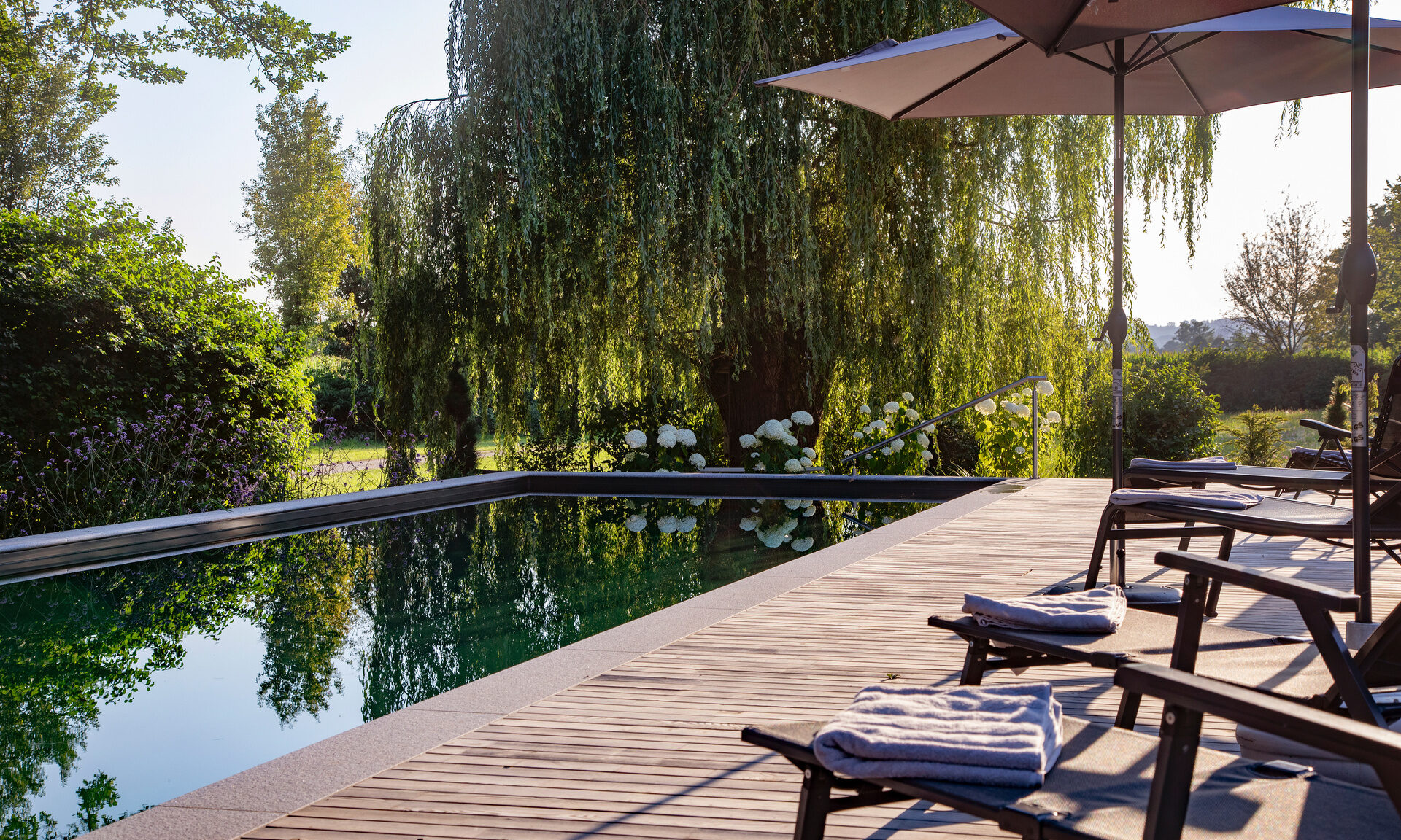 Die Holzterrasse mit Liegen und Sonnenschirmen beim Naturpool im Hotel Quellenhof im Rottal