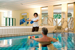 Ein Mann in einem Becken in der Rottal Terme führt Medical Wellness Übungen mit einer Trainerin aus.