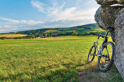 Ein Mountainbike lehnt an einer steinernen Mauer mit malerischer Wiese im Rottal im Hintergrund.