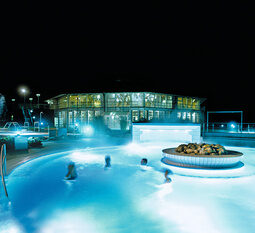 Das beleuchtete Aussenbecken der Rottal Terme bei Nacht, mit schwimmenden Besuchern.