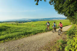 Drei Radfahrer fahren einen Weg entlang mit malerischer rottaler Landschaft im Hintergrund an einem schönen Sommertag.