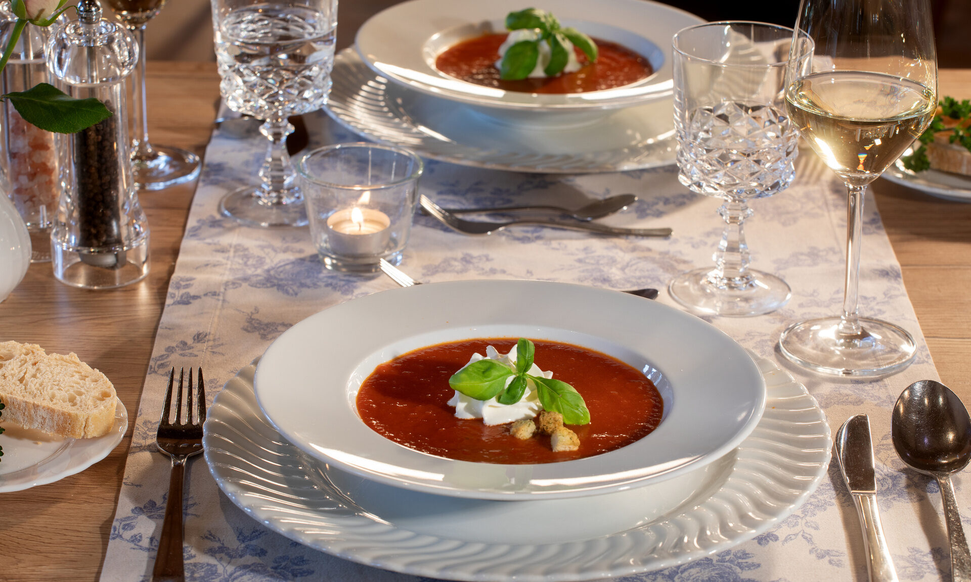 Schön garnierte Tomatensuppe auf weissen Teller mit einem Glas Weisswein im Restaurant Quellenhof.