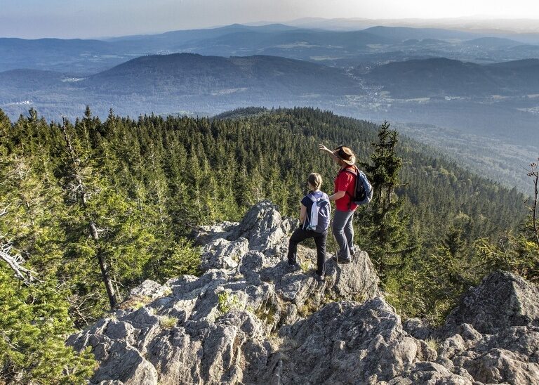 Zwei Wanderer im Nationalpark Bayerischer Wald stehen auf einem Stein und blicken über die Weiten des Bayerischen Waldes