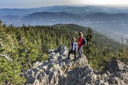Zwei Wanderer im Nationalpark Bayerischer Wald stehen auf einem Stein und blicken über die Weiten des Bayerischen Waldes