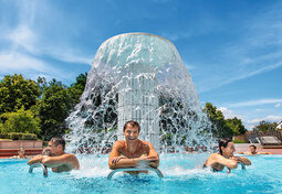 Eine Gruppe von Gästen genießen in einem Becken der Rottal Terme die Wasserfontäne die kühles Nass auf die Rücken spritzt.